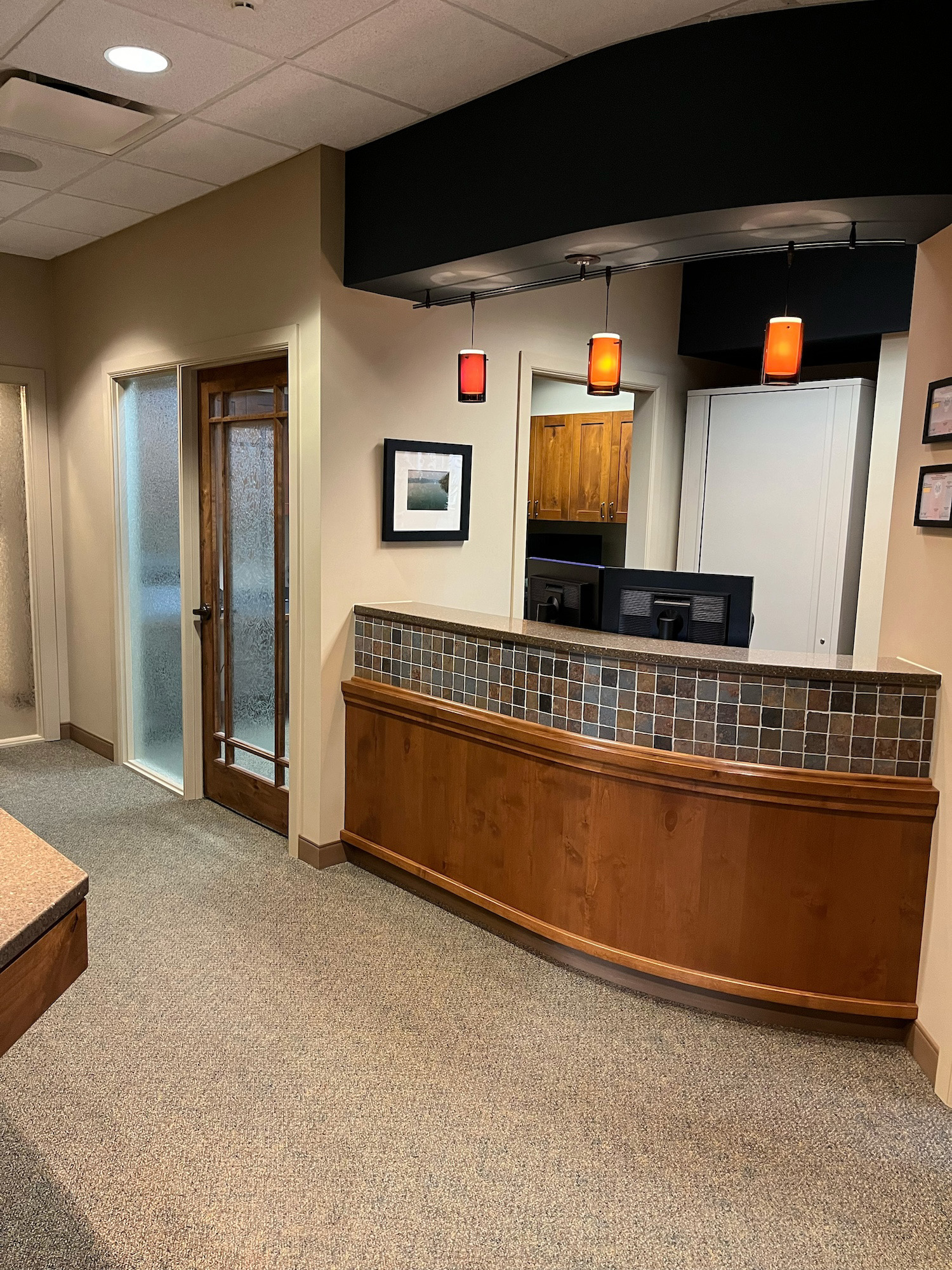 The image shows an interior view of a modern lobby with a reception counter, featuring a warm color palette and contemporary design elements.