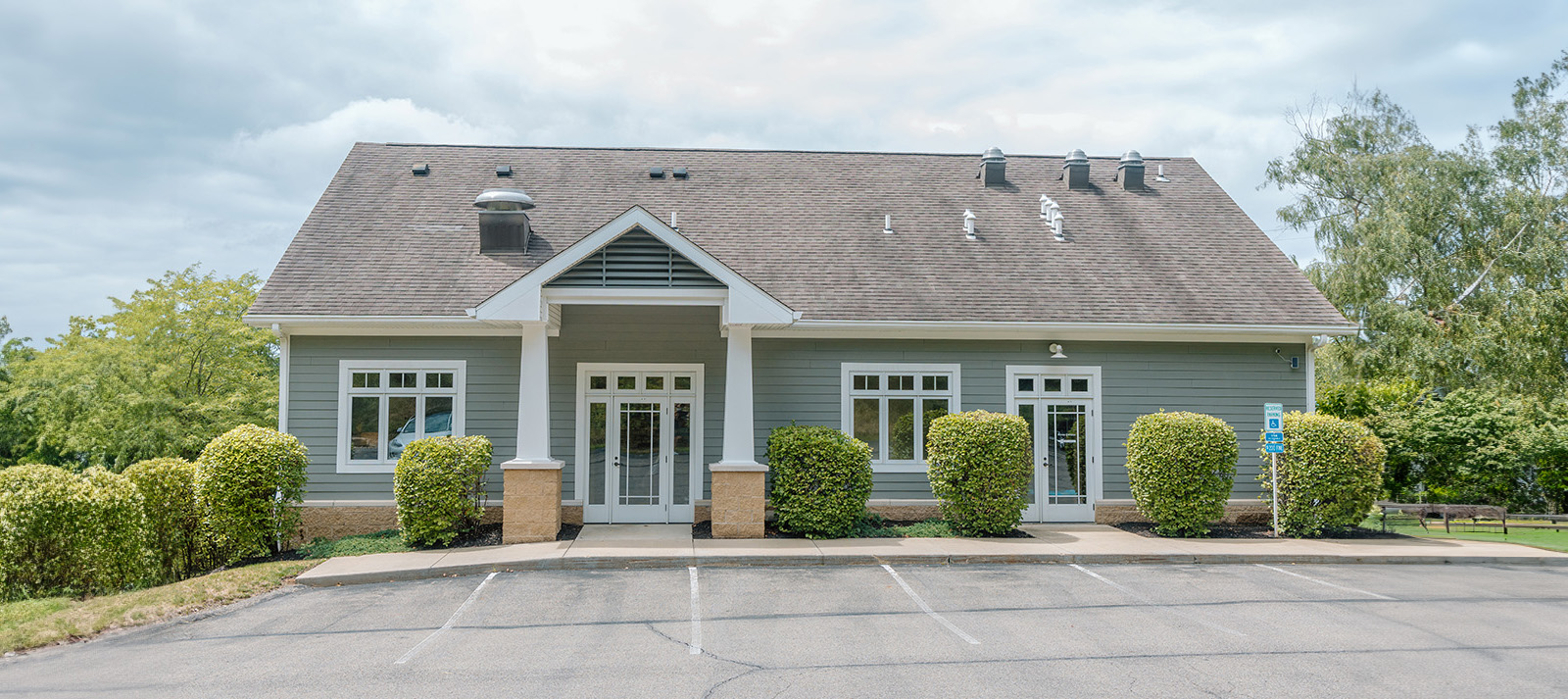 The image shows a two-story building with a flat roof, featuring a prominent front entrance and a small parking lot in the foreground.