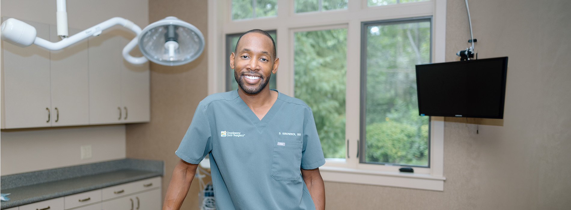 The image shows a person standing in an operating room, smiling at the camera.