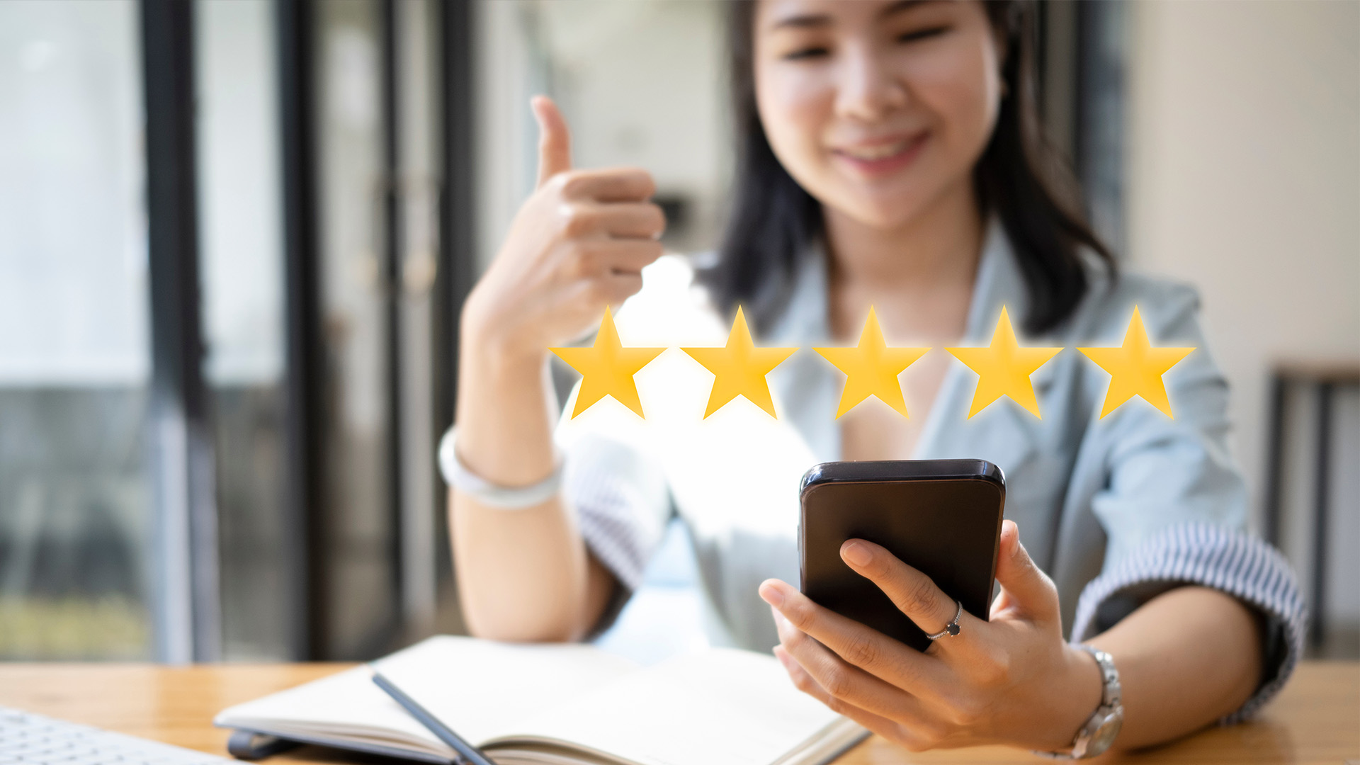 A woman is holding a smartphone and displaying five stars, possibly indicating her satisfaction with a service or product.