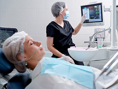 The image depicts a medical setting with a patient lying on a hospital bed and a healthcare professional standing next to it, both wearing protective face masks.