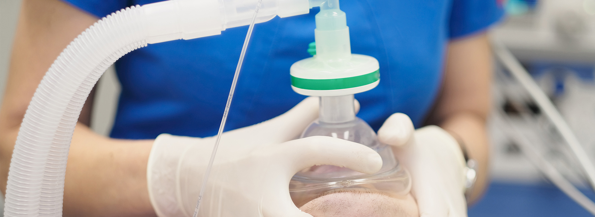 Woman in white gloves holding a clear plastic tube with a green cap, connected to a medical device.