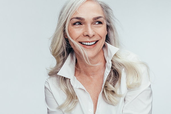 Woman with blonde hair smiling, wearing a white top and has her hair styled in an updo.